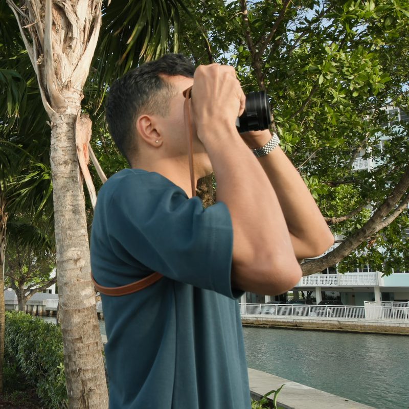 A man looking far ahead through binoculars on a riverside path